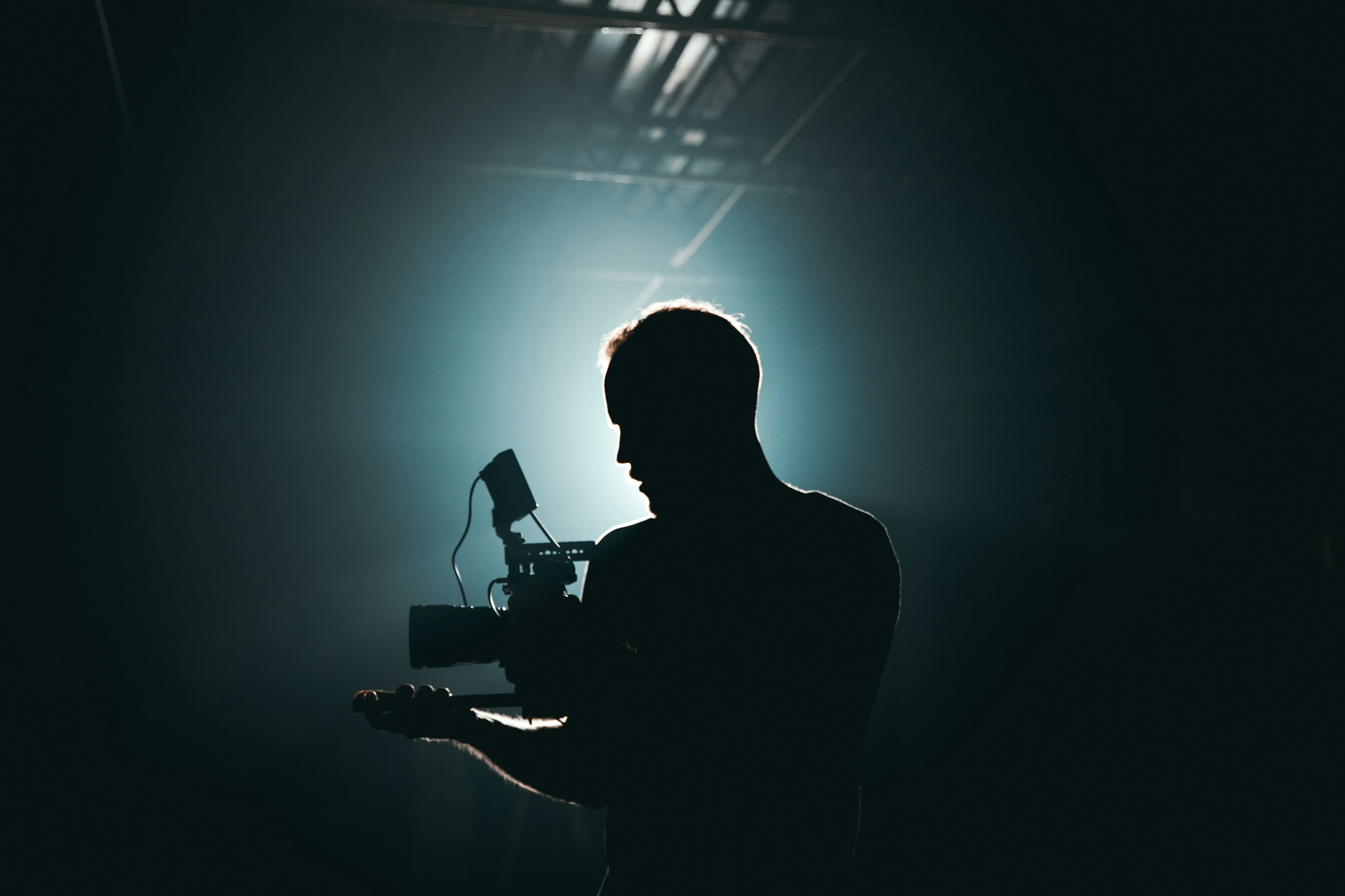 A silhouette of a filmmaker and tripod camera, backlit by a spotlight